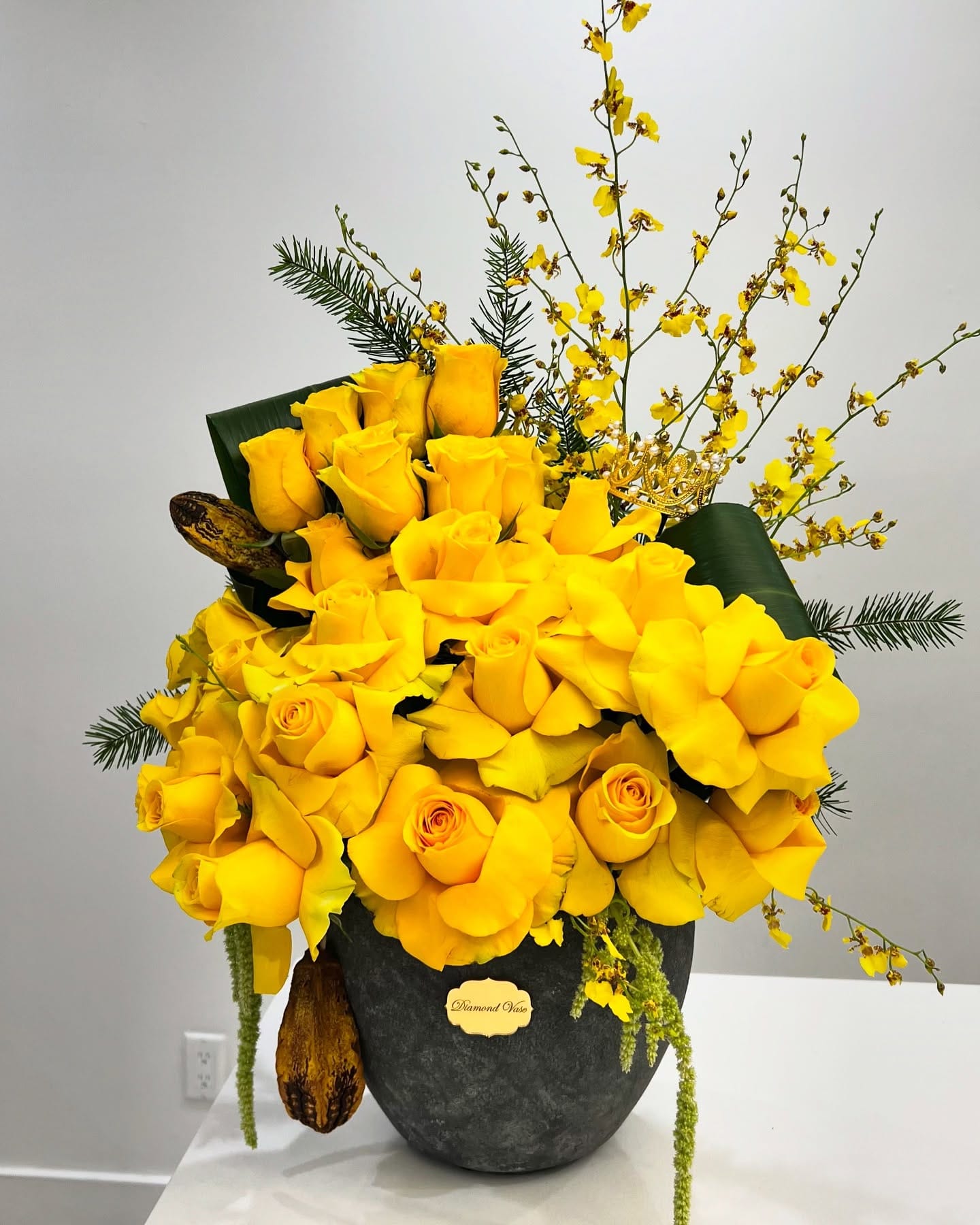 Mass of yellow roses with oncidium orchids and trailing amaranthus in a charcoal stone vase