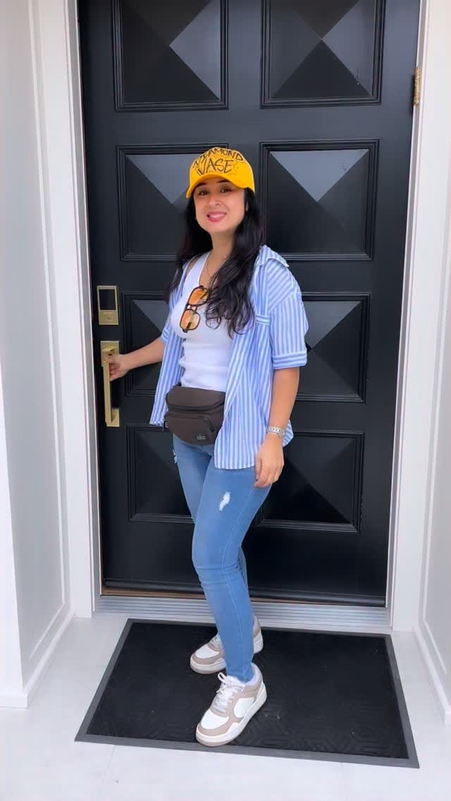 Bita in a yellow Diamond Vase cap, blue striped shirt and jeans posing at a black paneled front door.