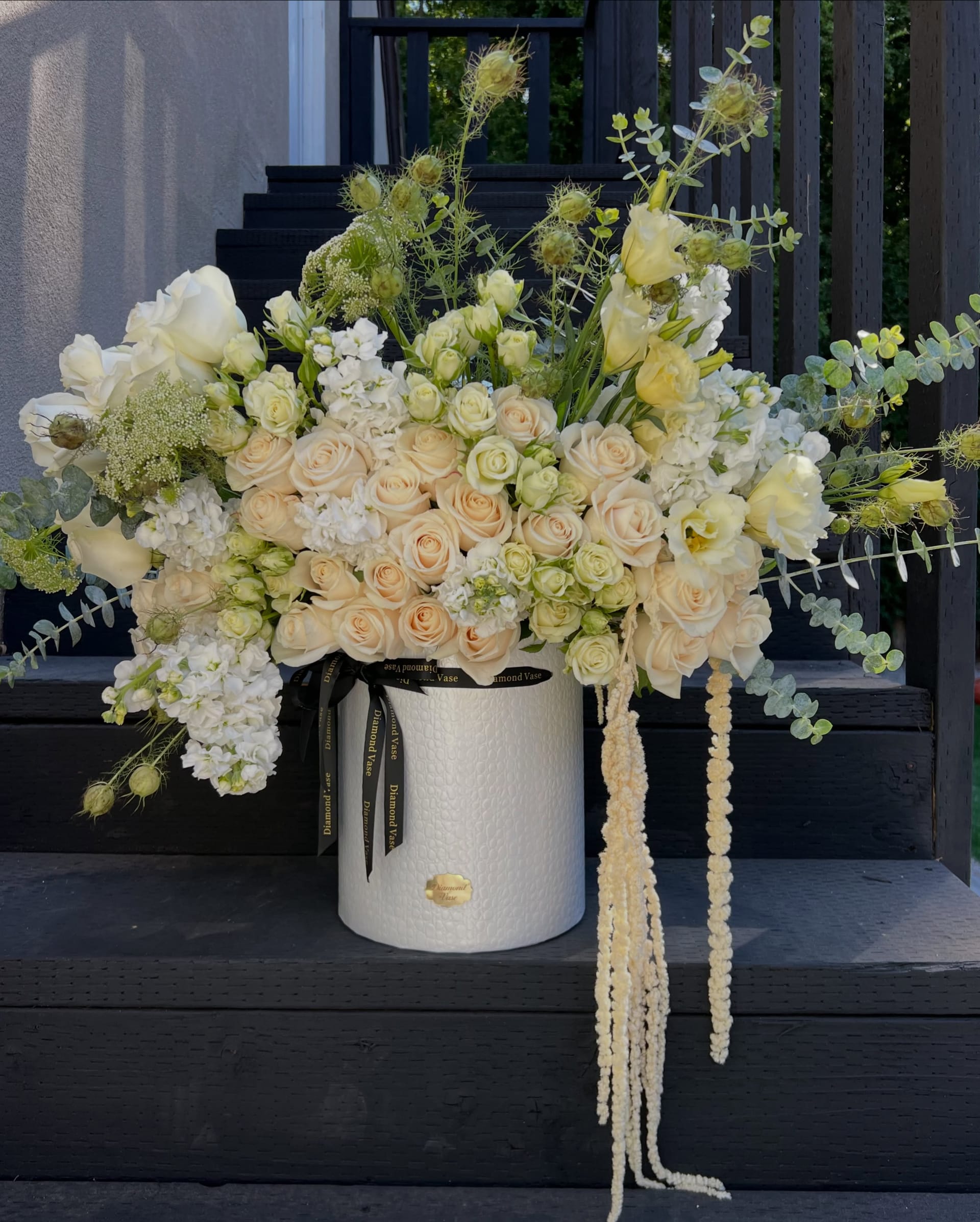 Ivory garden roses, white stock and trailing cream amaranthus in a textured Diamond Vase box on black stairs