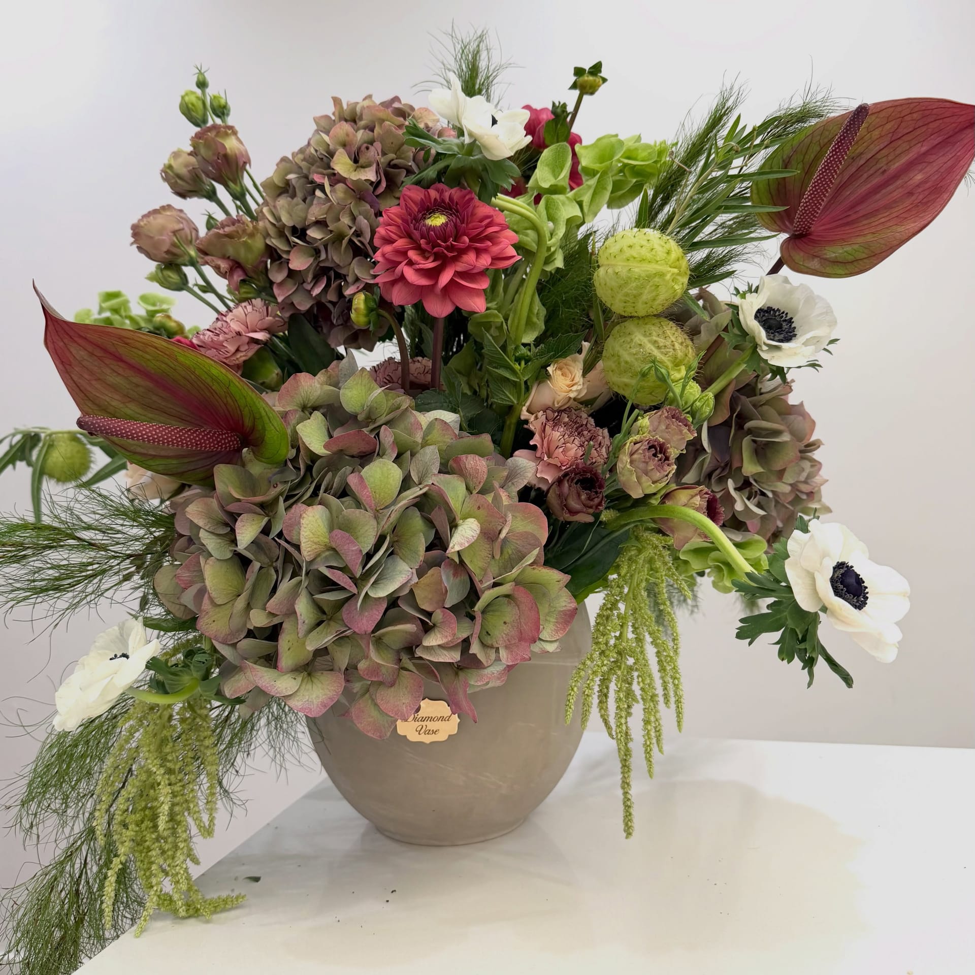 Autumn arrangement of antique hydrangea, burgundy dahlias and white anemones in a taupe stone urn