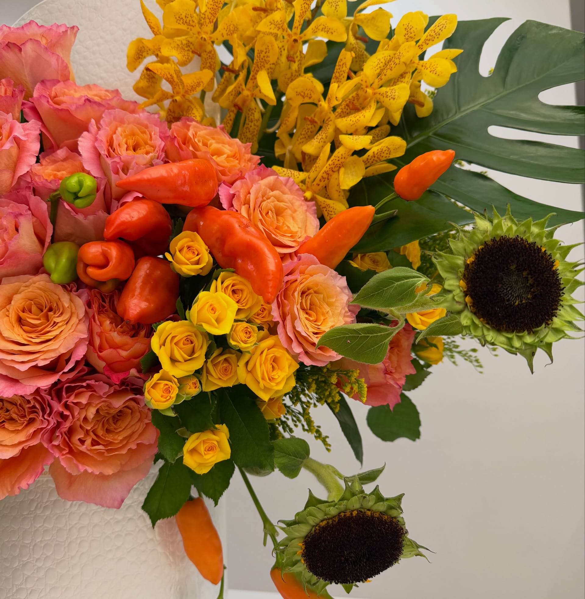 Close-up of orange peppers, spotted orchids and a monstera leaf in a fall arrangement